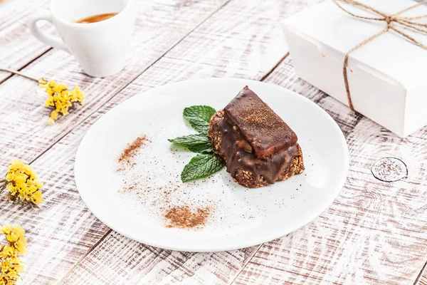 Close up view on vegan chocolate dessert with a cup of espresso on white wooden table. Fresh vegetarian dessert food for breakfast. Healthy meal with packing box. Copy space for design on box.