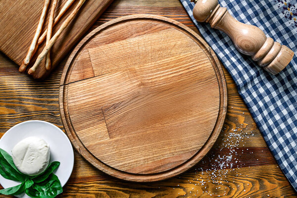 Empty food tableware. wooden cutting board for pizza with blue textile, mozarella, basil and pepper pot on wooden table. Restaurant, food menu, cafe concept. Free copy space for text. Top view