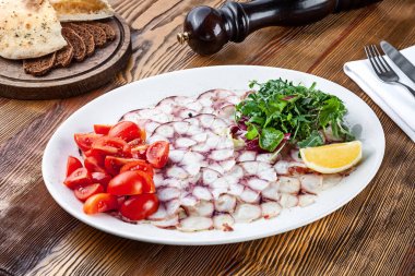 Beyaz plaka üzerinde ahtapot carpaccio lezzetli görünümü. Kopya alanı ile ahşap arka planda sos ile RAW ahtapot bonfile üzerinde görünüm yakın. Taze İtalyan mutfağı atıştırmalıkları. Deniz Mahsülleri İtalyan Akdeniz 