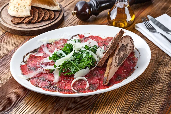 Close up view on veal carpaccio with parmesan and toast. Raw beef tenderloin with sauce on wooden background with copy space. Fresh italian cuisine snack — Stock Photo, Image