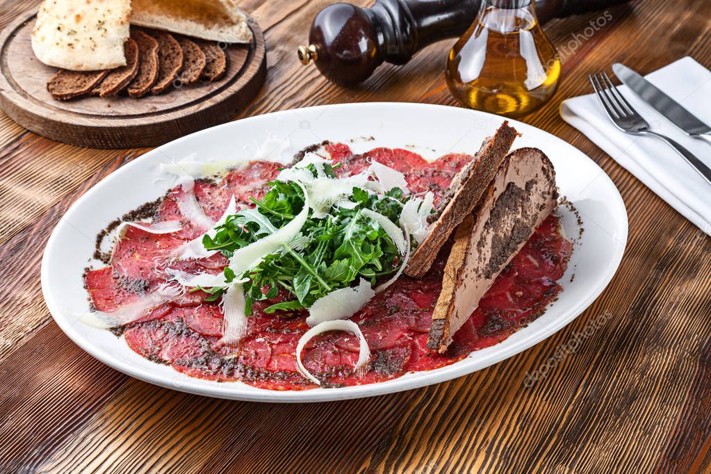 Close up view on veal carpaccio with parmesan and toast. Raw beef tenderloin with sauce on wooden background with copy space. Fresh italian cuisine snack