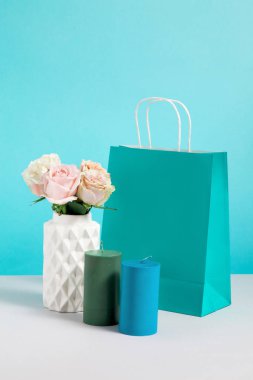 Vazo, mum ve kağıt torba çiçek ile hala hayat görüntü. Zanaat alışveriş çantaları mockup. Satış veya indirimler için konsept. Marka taklit. Mavi arka planda dekor dükkanı için kopya alanı ile görüntü