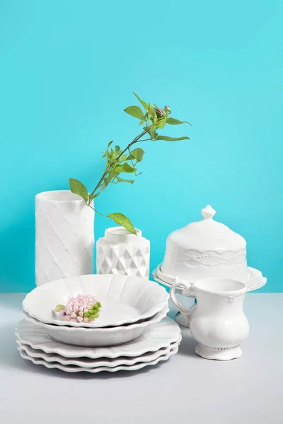 Mock up image with White tableware for serving and flower vases on grey table against blue background with space for design. Image for shops of ceramic tableware. Still life concept.