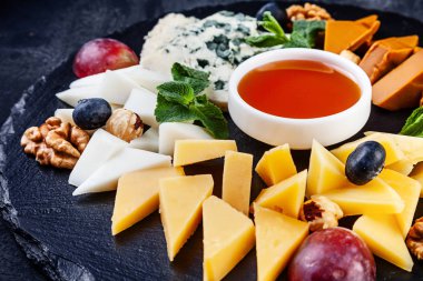 Fındık, üzüm, bal ile servis peynir tabağı üzerinde yakından görünümü. Kopyalama alanı ile koyu arka planda farklı peynir türlerine seçici odaklanma