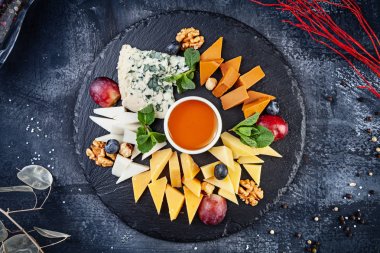 Fındık, üzüm, bal ile servis peynir tabağı üzerinde üst görünümü. Kopyalama alanı ile koyu arka planda farklı peynir türlerinde yukarıdan görüntüleyin