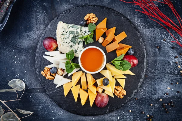 Top view on cheese plate served with nuts, grapes, honey. View from above on different types of cheese on dark background with copy space