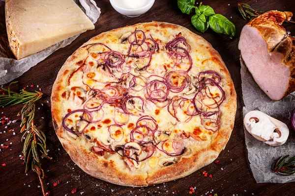 Top view on pizza with ham, onion and parmesan and white sauce with ingridients on brown wooden table. Picture for recipe or menu. Copy space for design. Served and cooked pizza. Italian cuisine