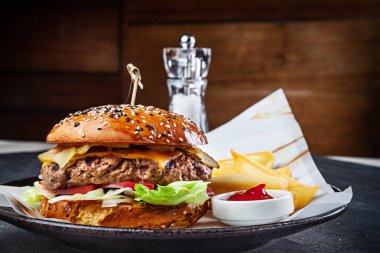 Sos ve patates kızartması ile servis edilen taze büyük burgerin yakından görünümü. Geleneksel Amerikan fast food'u. Marullu sulu çizburger, salatalık turşusu, domates. Kopyalama alanı