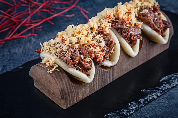 Primer plano en Gua bao, bollos al vapor con carne (veel). Bao servido con sabrosa cobertura sobre fondo oscuro. Cocina asiática. Sándwich asiático al vapor de guá bao. Estilo japonés de comida rápida — Foto de Stock