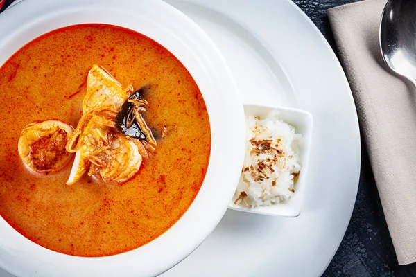 Draufsicht auf Tom-Yum-Suppe, serviert in weißem Teller mit Reis. Suppe mit Garnelen, Meeresfrüchten, Kokosmilch und Chili in Schüssel Kopierraum. traditionelle thailändische Küche. Mittagessen mit Kopierraum — Stockfoto