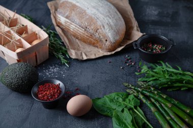 Yemek pişirmek için ingridients. Taze, organik sebzeler, glutensiz ekmek, eko yumurta ve maydanoz. bahar sebzeler, kopya alanı ile koyu taş arka plan üzerinde avokado. Düz yatıyordu. Sağlıklı gıda kavramı