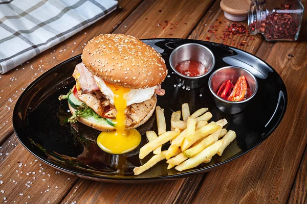 Świeży Burger z jajkiem kurczaka, sałata i sos na czarnej płycie z frytkami. Amerykańskie Fast food. Chickenburger z kopią miejsca na drewnianym tle. Zbliżenie, selektywne skupienie. Żywności. Menu grilla — Zdjęcie stockowe