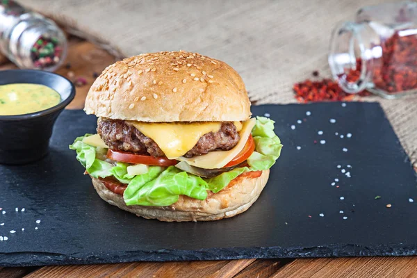 Hambúrguer saboroso fresco com queijo, alface, tomate, pepino em pedra preta com molho. Fast food americano. Cheeseburger com espaço de cópia em fundo de madeira. Fechar, foco seletivo. Comida. Menu Grill — Fotografia de Stock