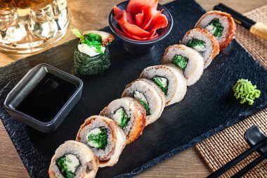 Suşi rulo seti yakın görünüm. Yılan balığı, avokado ve havyar ile Kaliforniya rulo ahşap masada siyah taş üzerinde hizmet vermiştir. Japon mutfağı. Boşluk Kopyala. Menü için suşi servis edildi. Sağlıklı gıda, deniz ürünleri