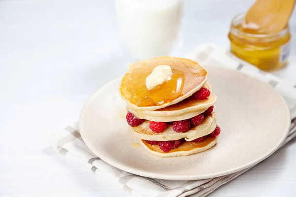 Nahaufnahme auf einem Stapel frischer, hausgemachter Pfannkuchen mit Himbeeren, schmelzender Butter und dem Gießen von Honig oder Marmorsirup. Amerikanischer Pfannkuchen auf weißem Hintergrund mit Morgenlicht. Frühstück. Selektiver Fokus. — Stockfoto