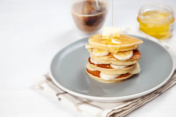 Nahaufnahme auf einem frischen, hausgemachten Pfannkuchenstapel mit Banane, schmelzender Butter und Honig oder Marmorsirup. amerikanischer Pfannkuchen mit einem Glas Kaffee mit Morgenlicht. Frühstück Essen mit Kopierraum — Stockfoto