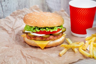 Zanaat kahverengi kağıt üzerinde patates kızartması ile Burger görünümü yakın. Geleneksel Fast-Food. marul, domates, peynir ve salatalık ile taze lezzetli çizburger. Tasarım için alanı kopyalayın. Sağlıksız yiyecekler. Yağ