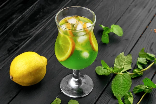 Glass of cold green cocktail with lemon and mint. Mojito. Summer freshness lemonade with ice. Dark background. Copy space.