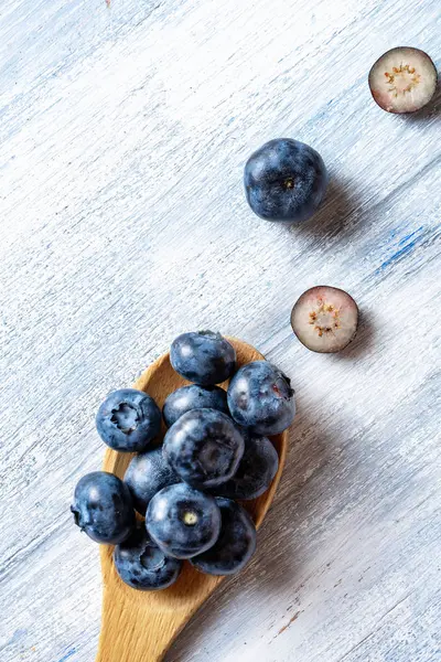 Vista superior en arándano en una cuchara de madera sobre fondo rústico azul. Concepto alimenticio de fruta natural. La mitad del arándano plano yacía. Diseño creativo. Vertical. espacio de copia — Foto de Stock