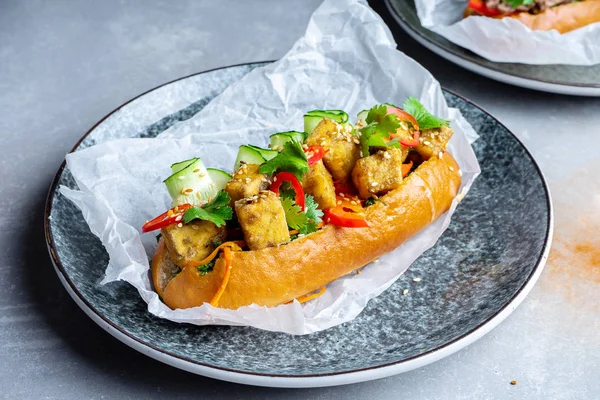 Pan-asian cuisine. traditional banh-mi sandwich with grilled tofu cheese, parsley, cucumber, chili pepper. street food on grey stone background. bahn mi. Vegan, healthy fast food