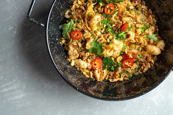 Draufsicht auf Pad Thai, oder Phad Thai gebratene Reisnudeln mit Gemüse und Huhn, scharfer Chilischote und Petersilie in schwarzer Schüssel auf grauem Steingrund. Straße panasiatisches Essen mit Kopierraum — Stockfoto