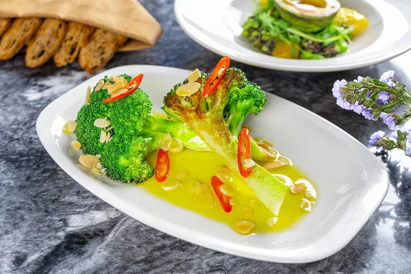 Flat lay food. Close up view on delicious fried broccoli with chili and butter served on white plate on marble table. Modern cuisine. Healthy food. Green food. Restaurant photo for menu or poster