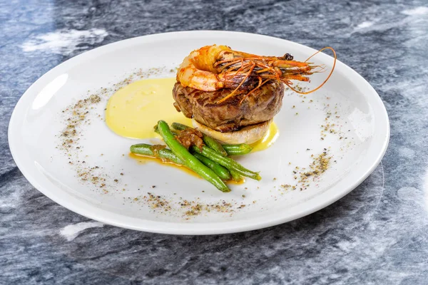 Close up view on Filet Mignon with tiger shrimp, asparagus and mashed potato on white plate. Restaurant luxury food on marble table. Medium rare beef steak with shrimp. Seafood and meat — Stock Photo, Image