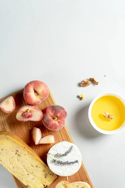 Vista superior de diferentes tipos de quesos en tabla de cortar de madera. Queso con higo melocotón, miel, ciabatta y nueces, copa de vino tinto. Elegante comida plana yacía sobre fondo gris. Copiar espacio. Enfoque suave — Foto de Stock