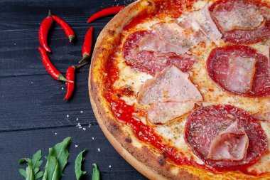 Koyu ahşap arka plan üzerinde salam, acı biber biber, jambon ve peynir ile üst görünüm pizza. Tasarım için sapce kopyalayın. Yemek geçmişi. İtalyan mutfağı. Düz lay gıda