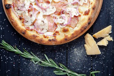 Koyu ahşap arka plan üzerinde jambon, mantar ve peynir parmesan ile üst görünüm pizza. Tasarım için sapce kopyalayın. Yemek geçmişi. İtalyan mutfağı. Düz lay gıda