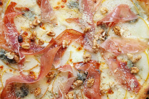 Close up view on texture pizza with jamon, gorgonzola and parmesan cheese, nuts and pear. Top view. Fresh homemade italian pizza. Food background. Pizza with meat and cheese