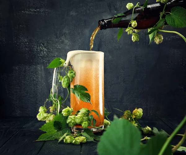 Kreativ collage öl från flaska hälls i ett glas. Begreppet naturöl. Hop wraps glas och flaska. Stilleben med öl och humle på mörk bakgrund. Kreativ affisch. Flygande vätska — Stockfoto