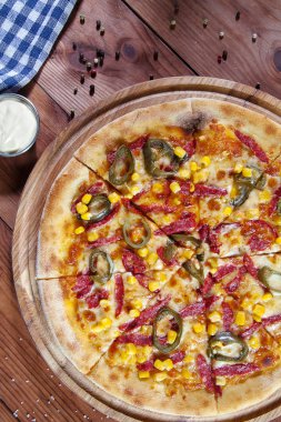 Üst görünümü ahşap arka plan üzerinde mısır, salam ve kırmızı sos ile sıcak biber pizza. Gıda düz yatıyordu. Kopya alanı. İtalyan mutfağı. Taze ev yapımı dilimlenmiş pizza