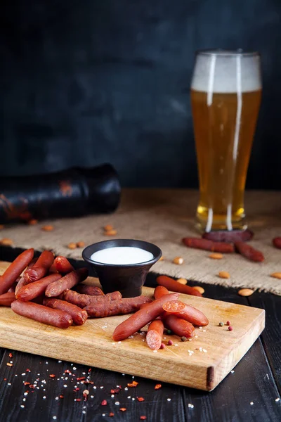 Närbild på korv. Välsmakande ölsnack Wurst salami. aptitretande ölsnack sekektiv fokus. Bord med salami korv, vit sås och glas öl. Mörk bakgrund — Stockfoto