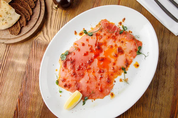 Top uitzicht op zalm carpaccio met rode kaviaar in witte plaat op houten achtergrond. Platte lay eten. Traditionele Italiaanse cusine zeevruchten. Voedsel foto voor achtergrond. Kopieer ruimte. Rauwe vis — Stockfoto