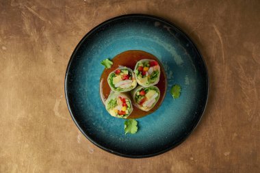 Karides, mango, salatalık ve acı soslu dolmalık biber ile iştah açıcı börekler. Bakır arka planda mavi bir seramik tabakta.