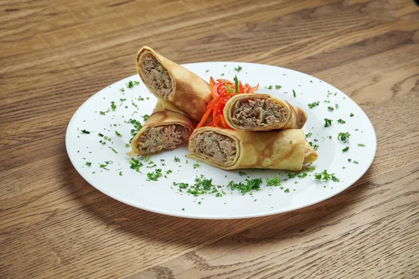 Klasik Ukrayna krepleri (krepler). Beyaz bir tabakta, ahşap bir zeminde ördek etiyle doldurulmuş. Görünümü kapat, seçici odak