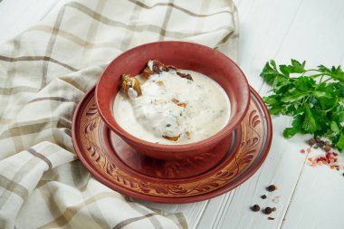 Gürcistan mutfağından iştah açıcı Chkmeruli tabağı. Ekşi krema soslu tavuk, beyaz ahşap arka planda seramik bir kasede sarımsak. Kapat.