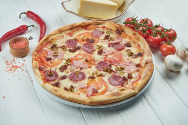 Klasik İtalyan pizzası, mozarella, domates, zeytin, mantar, salam ve jambon karışımı beyaz ahşap bir arka planda..