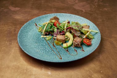 Izgara ton balığı, roka, vişneli domates, avokado ve salatalık mavi seramik tabakta, metal zemin. Kapatın. Deniz ürünleri salatası