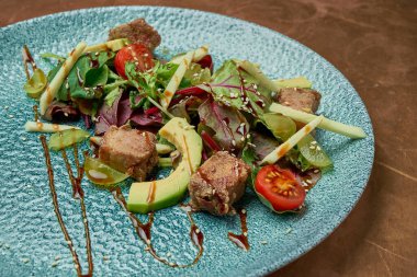 Izgara ton balığı, roka, vişneli domates, avokado ve salatalık mavi seramik tabakta, metal zemin. Kapatın. Deniz ürünleri salatası