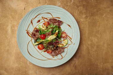 Izgara biftek, roka, vişneli domates, bakır kaplama beyaz seramik tabakta avokado. Kapatın. Sıcak et salatası.