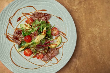 Izgara biftek, roka, vişneli domates, bakır kaplama beyaz seramik tabakta avokado. Kapatın. Sıcak et salatası.