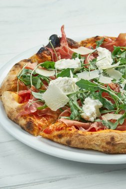 Beyaz ahşap bir tabakta jambon, parmesan, roka ve strakcella peynirli ev yapımı pizza.