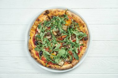 Zeytinli, erimiş peynirli, roka, mantar, beyaz ahşap arka planda beyaz bir tabakta kiraz domatesli ev yapımı vejetaryen pizzası.