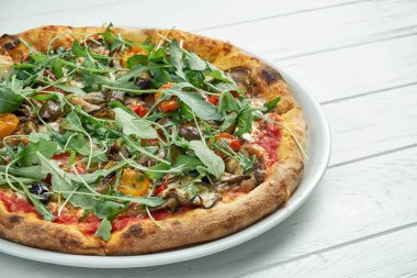 Zeytinli, erimiş peynirli, roka, mantar, beyaz ahşap arka planda beyaz bir tabakta kiraz domatesli ev yapımı vejetaryen pizzası.