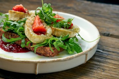Keçi peyniri, kırmızı reçel, roka ve ahşap bir zeminde çavdar ekmekli çilekli iştah açıcı tost.