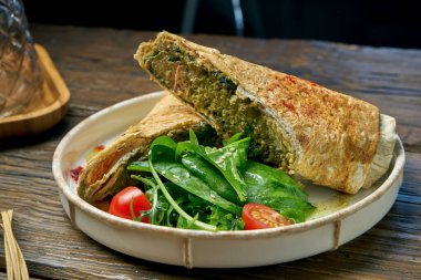 Tahta bir arka planda ıspanak, domates, humus ve erimiş peynirli vejetaryen shawarma dürümü.