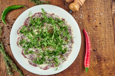Parmesan ve roka soslu sığır eti carpaccio 'nun üst görüntüsü. Ahşap arka planda soslu çiğ sığır filetosu. Lezzetli İtalyan mutfağı.