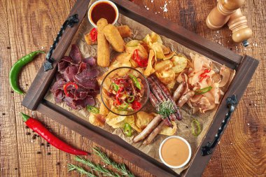 Çeşitli bira aperatifleri. Ahşap tepside sosis, cips, kurutulmuş et. Üst görünüm